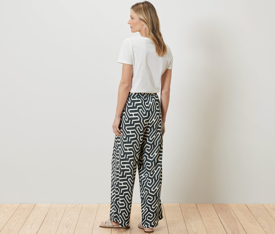 Egy nő háttal áll a kamerának, fehér pólót és nyomott mintás, gyűrött hatású belebújós nadrágot visel.