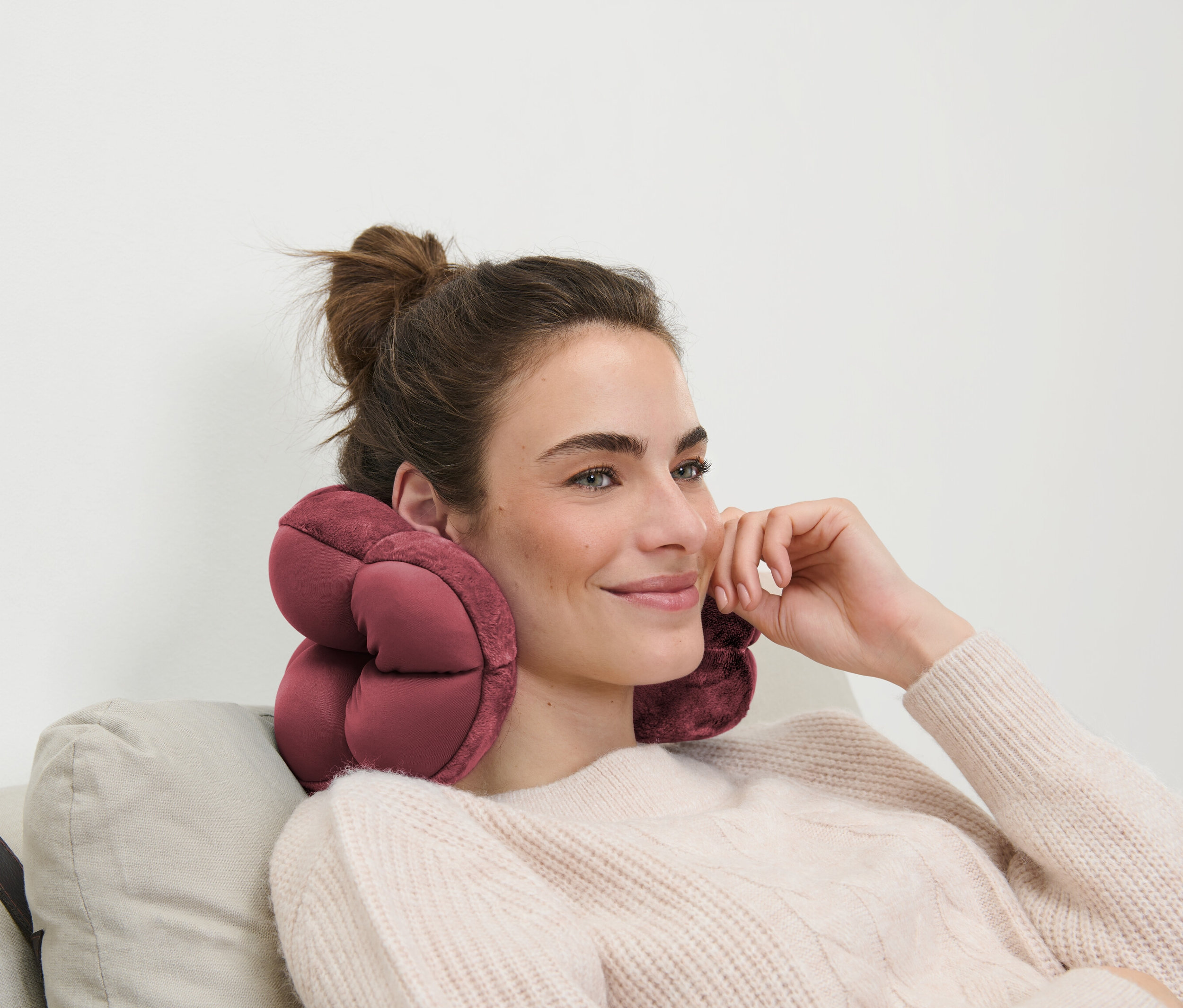 Barna hajú nő ül egy kanapén, rózsaszín utazópárna van a nyakában.