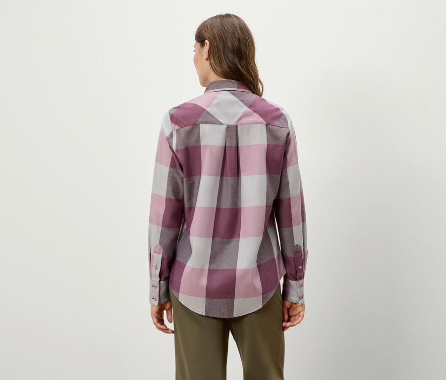 Hátulról látható egy nő kockás, hosszú ujjú ingben és zöld nadrágban.