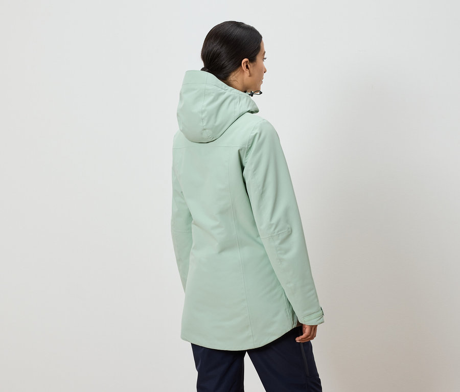 Hátulról látható egy nő mentazöld kapucnis kabátban és sötétkék nadrágban.