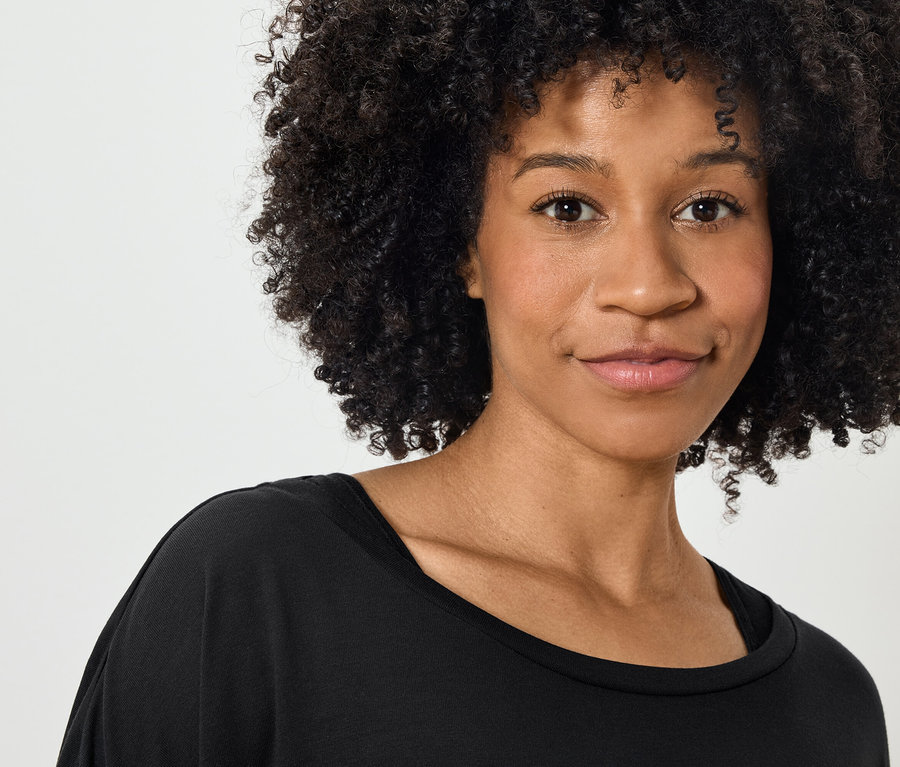 Portré egy mosolygó, göndör hajú nőről fekete pólóban.