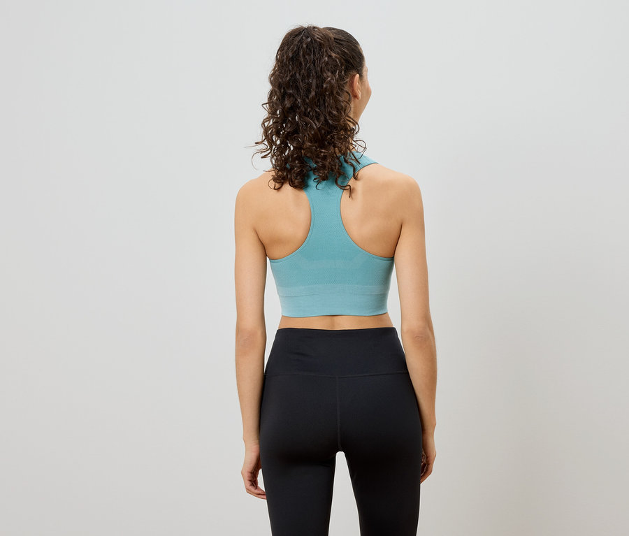Hátulnézet egy göndör hajú nőről, aki türkiz színű sportmelltartót és fekete leggingset visel.