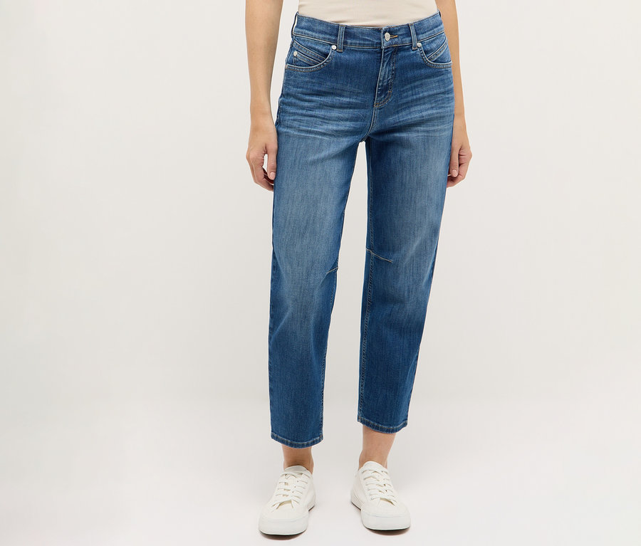 Egy személy kék Angels Denim »Evi« farmert és fehér cipőt visel fehér háttér előtt.