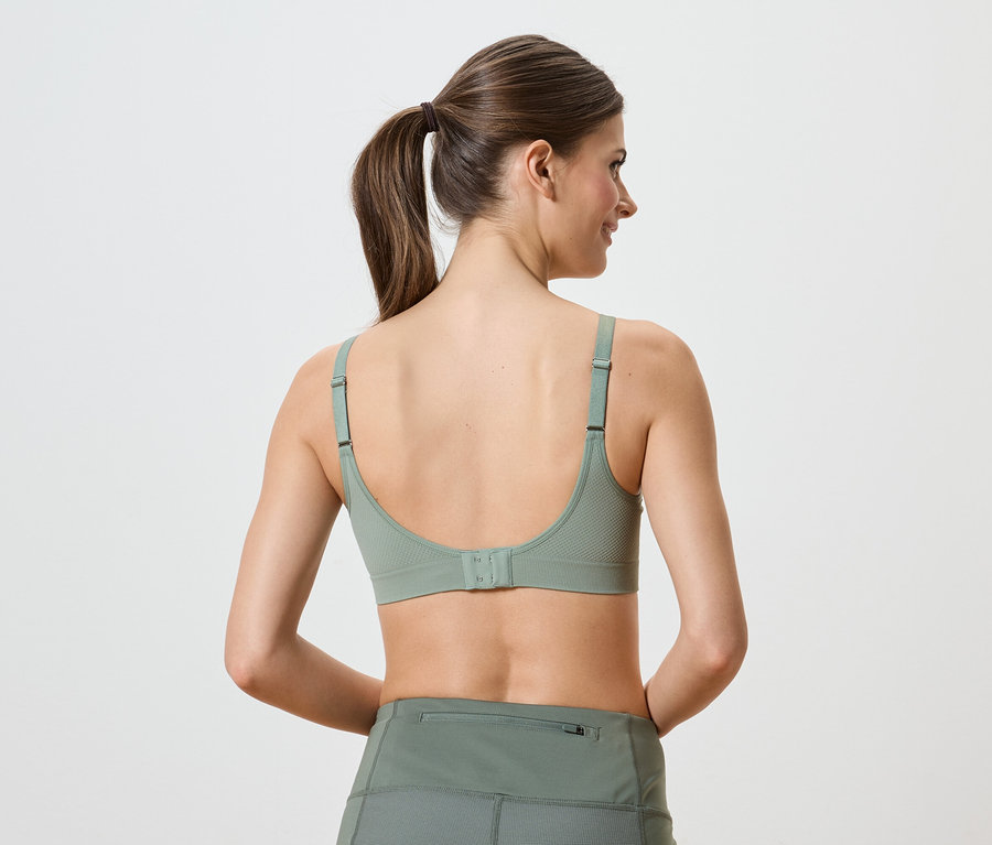 Hátulnézet egy zöld sportmelltartót és leggingset viselő, lófarokba kötött hajú nőről.
