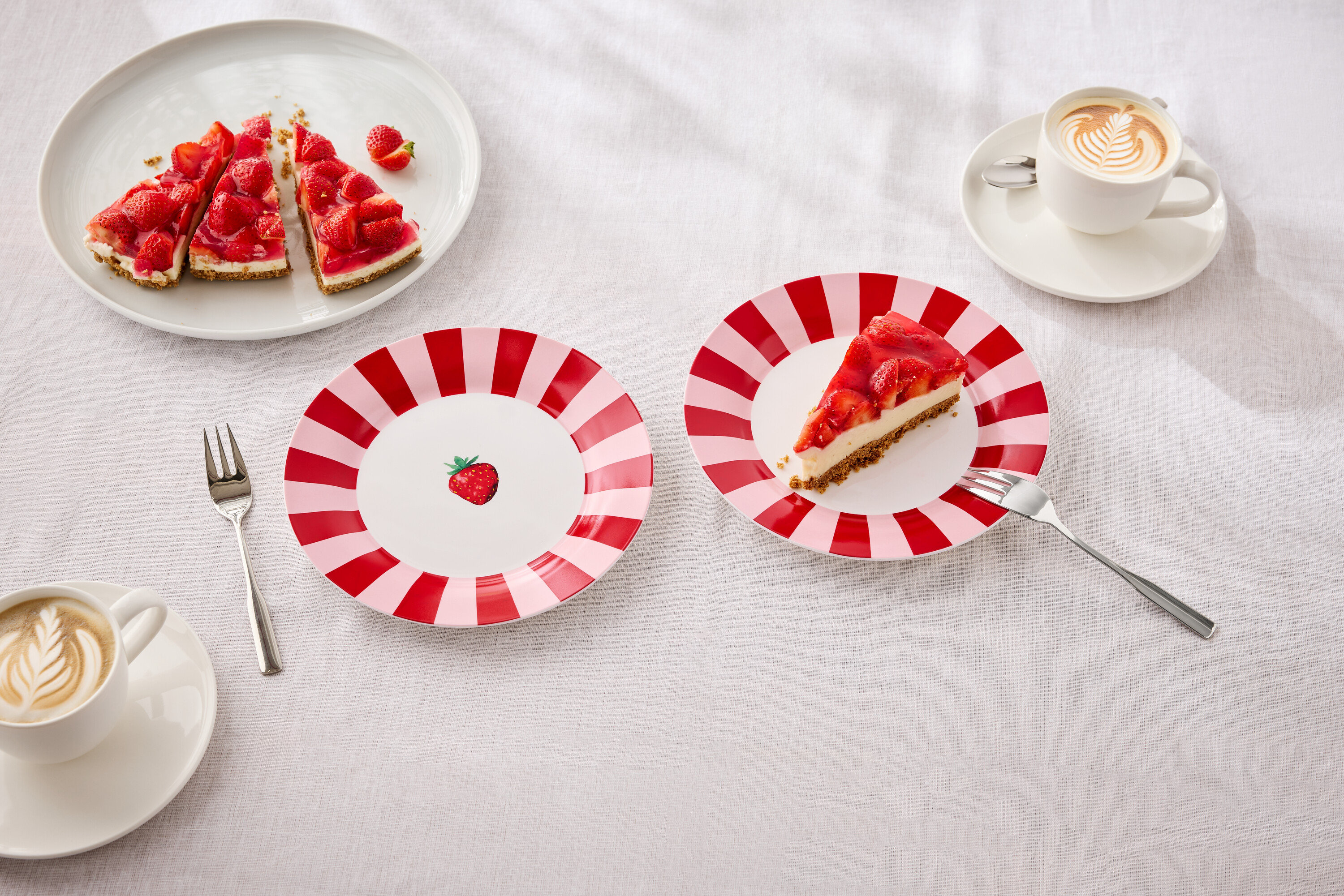 Az asztalon tányérok epertortával, villák és latte artos csészék találhatók.