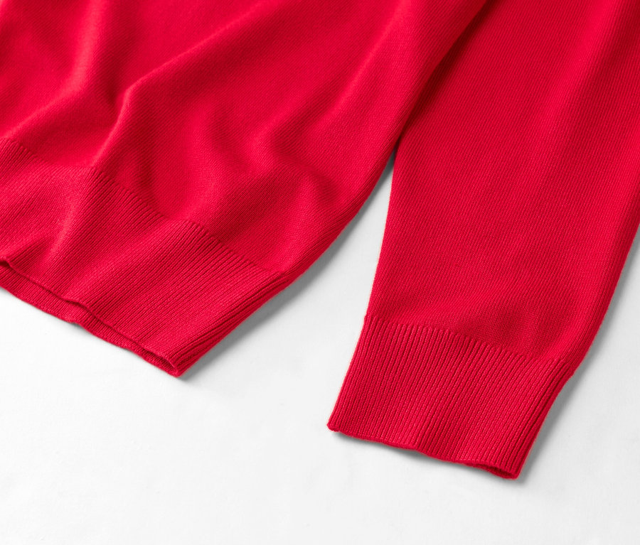 Egy piros pulóver részletének képe fehér háttér előtt.