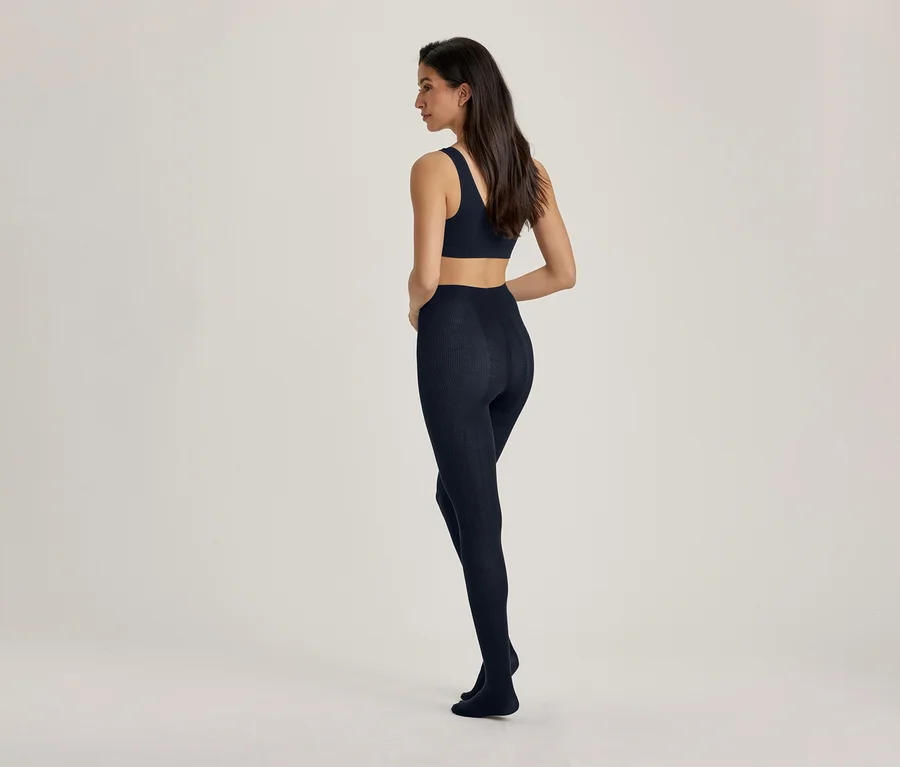 Egy nő háttal áll a nézőnek, enyhén balra fordulva, sötétkék sportmelltartót és hozzá illő sötétkék leggingset visel.