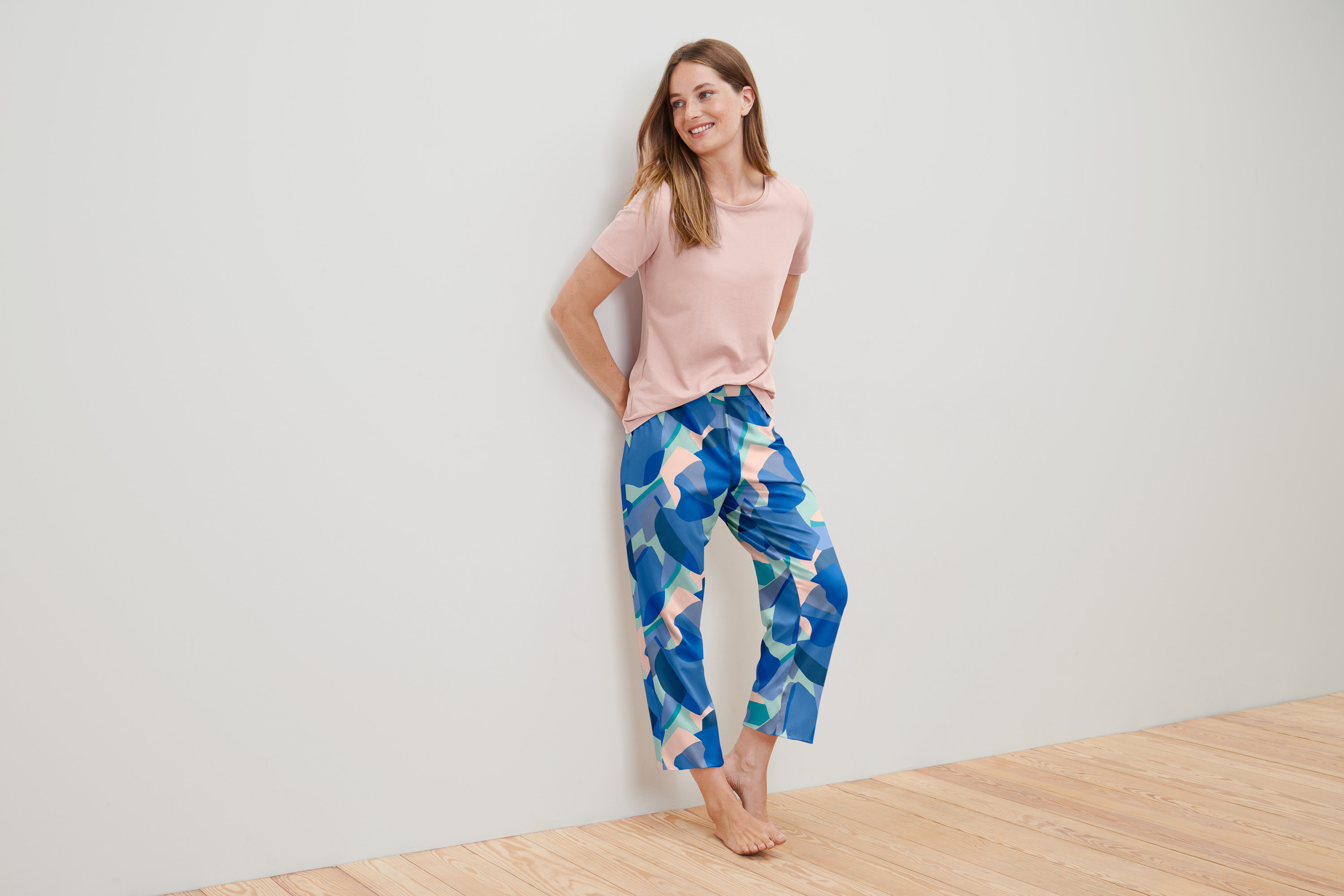 Falnak támaszkodó nő mintás, rózsaszín női 7/8-os pizsamában.