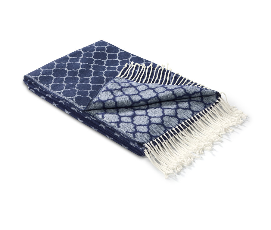 Egy részben összehajtott kék jacquard takaró fehér rojtokkal.