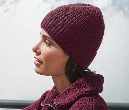 Egy nő ül kint és bordó kötött sapkát visel.
