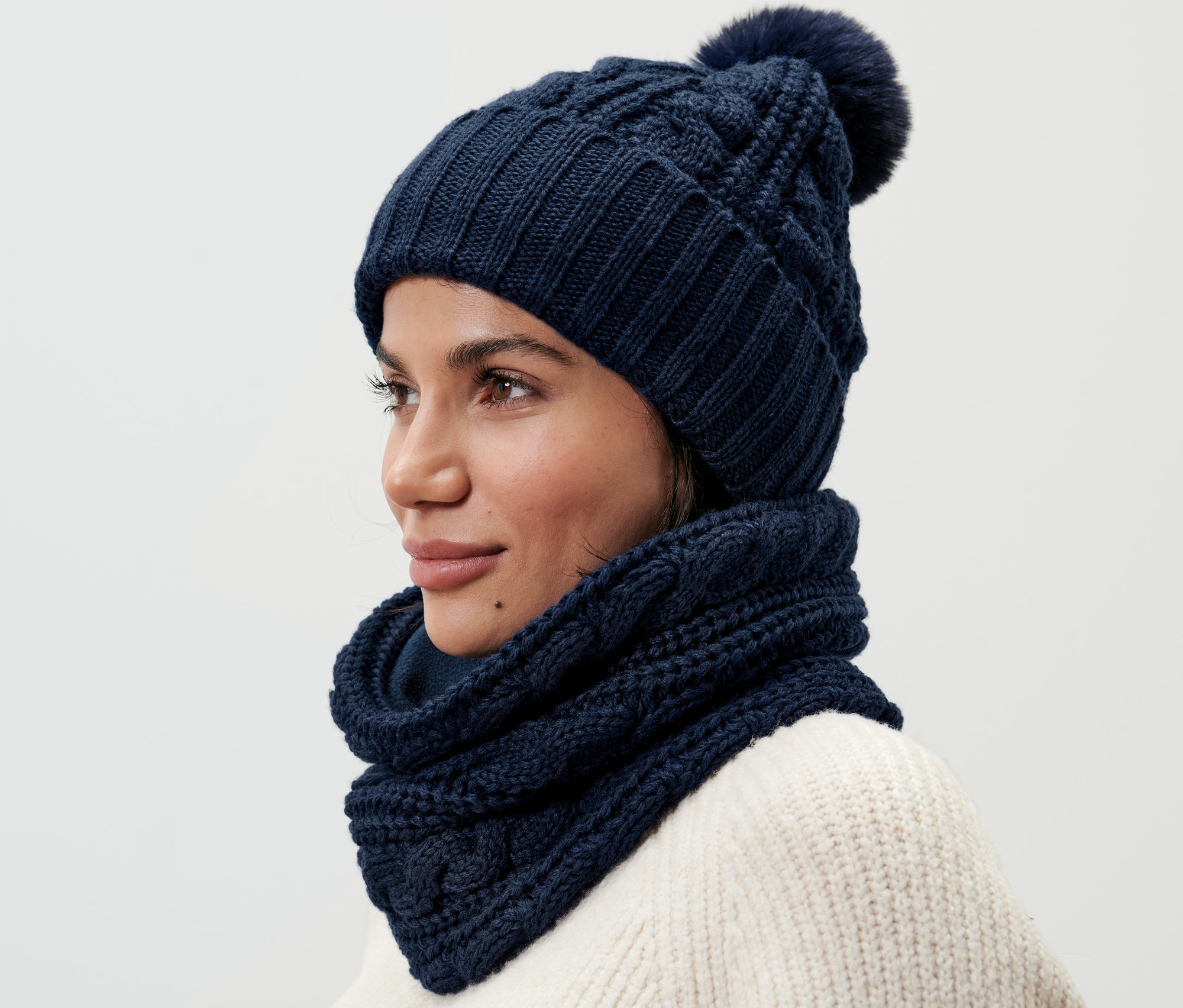Nő visel sötétkék kötött csősált és hozzáillő kötött sapkát.