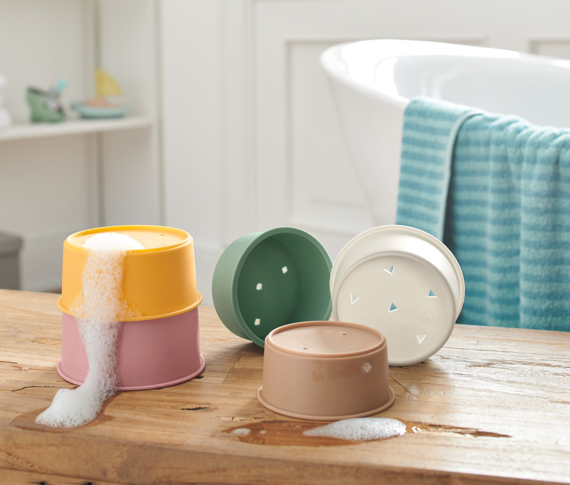 Egy fa asztalon összerakható játékvödrök láthatóak, kettő egymásra helyezve, a felső vödörből hab folyik ki.