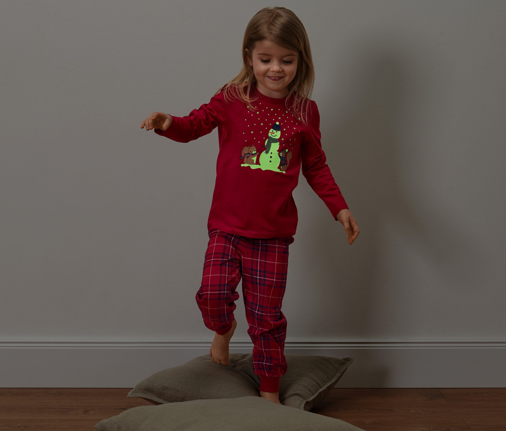 Kislány egyensúlyoz a párnákon, sötétben világító kisgyerek pizsamában.