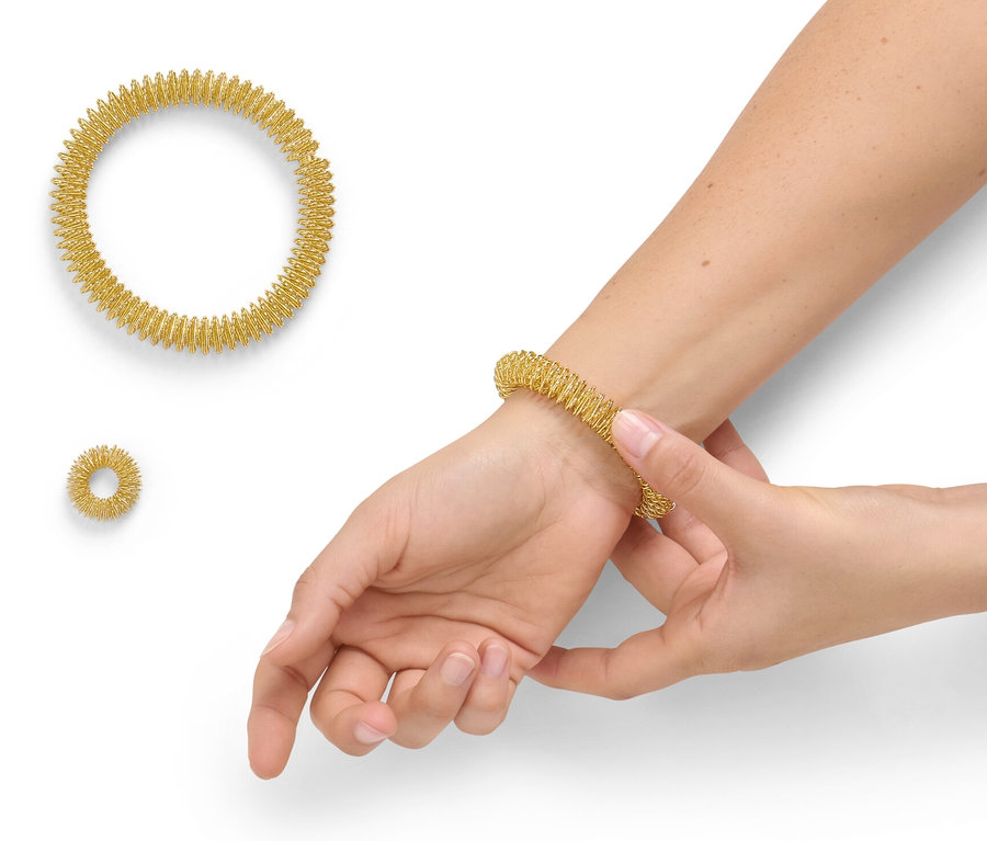 Egy nő egy arany akupresszúrás gyűrűt húz a csuklójára az akupresszúrás készletből. Két másik gyűrű mellette fekszik.