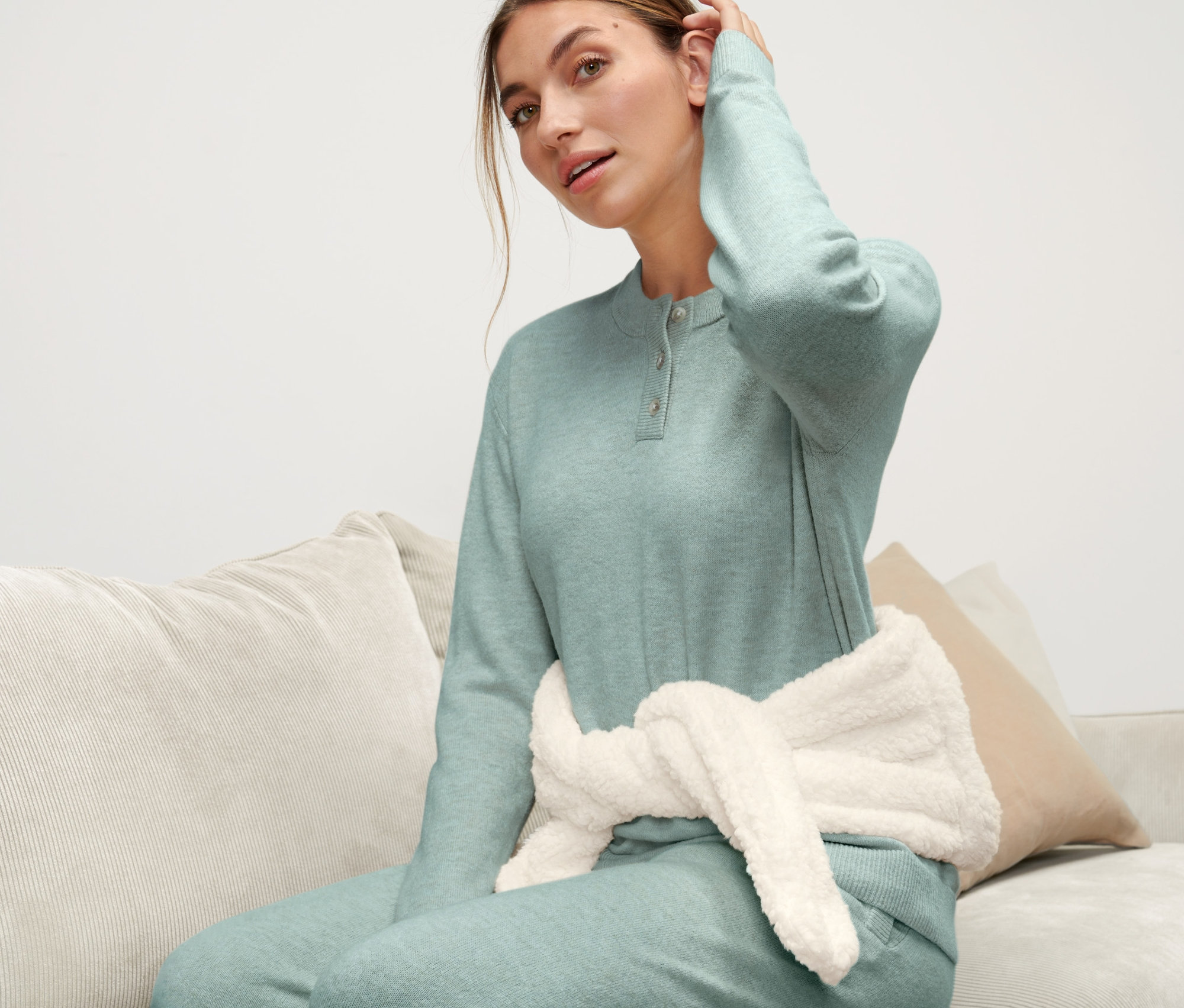 Nő ül a kanapén, derekán melegvizes palack pánttal.