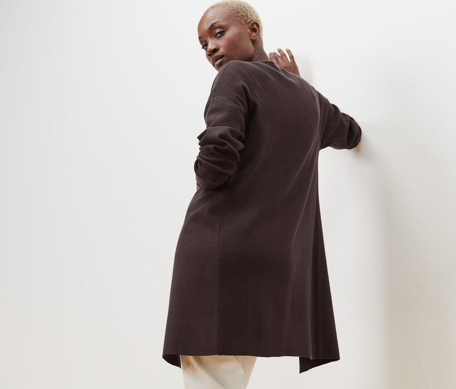 Egy nő a válla fölött hátra néz, és egy nyitott, barna kardigánt visel.