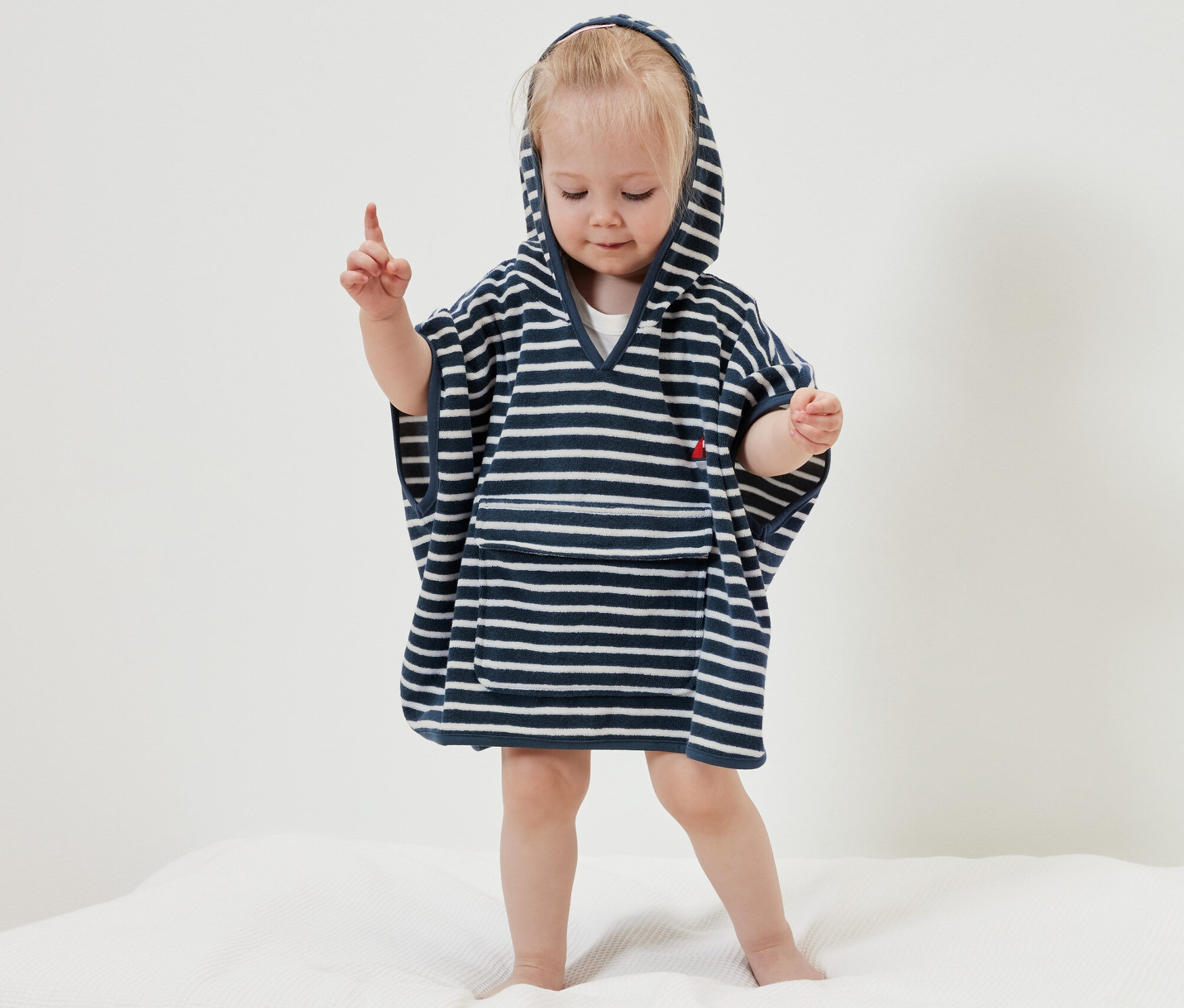 Egy kislány áll egy fehér takarón, és egy tengerész témájú frottírponcsót visel.