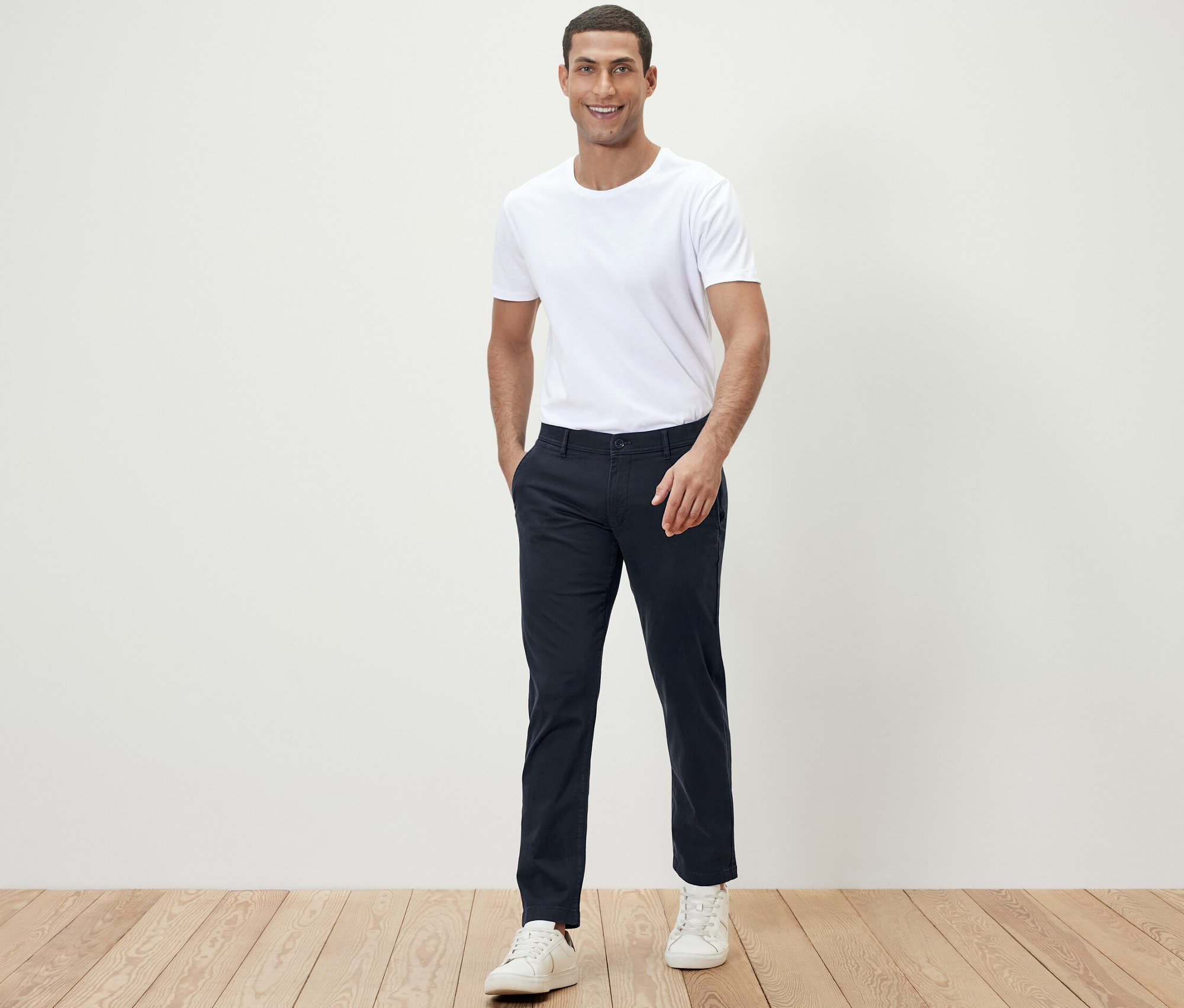 Férfi pózol a kamerának fehér pólóban és sötétkék chino nadrágban.