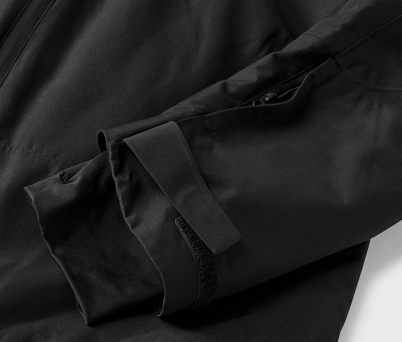 Egy fekete kabát részlete, ujjal és cipzárral.