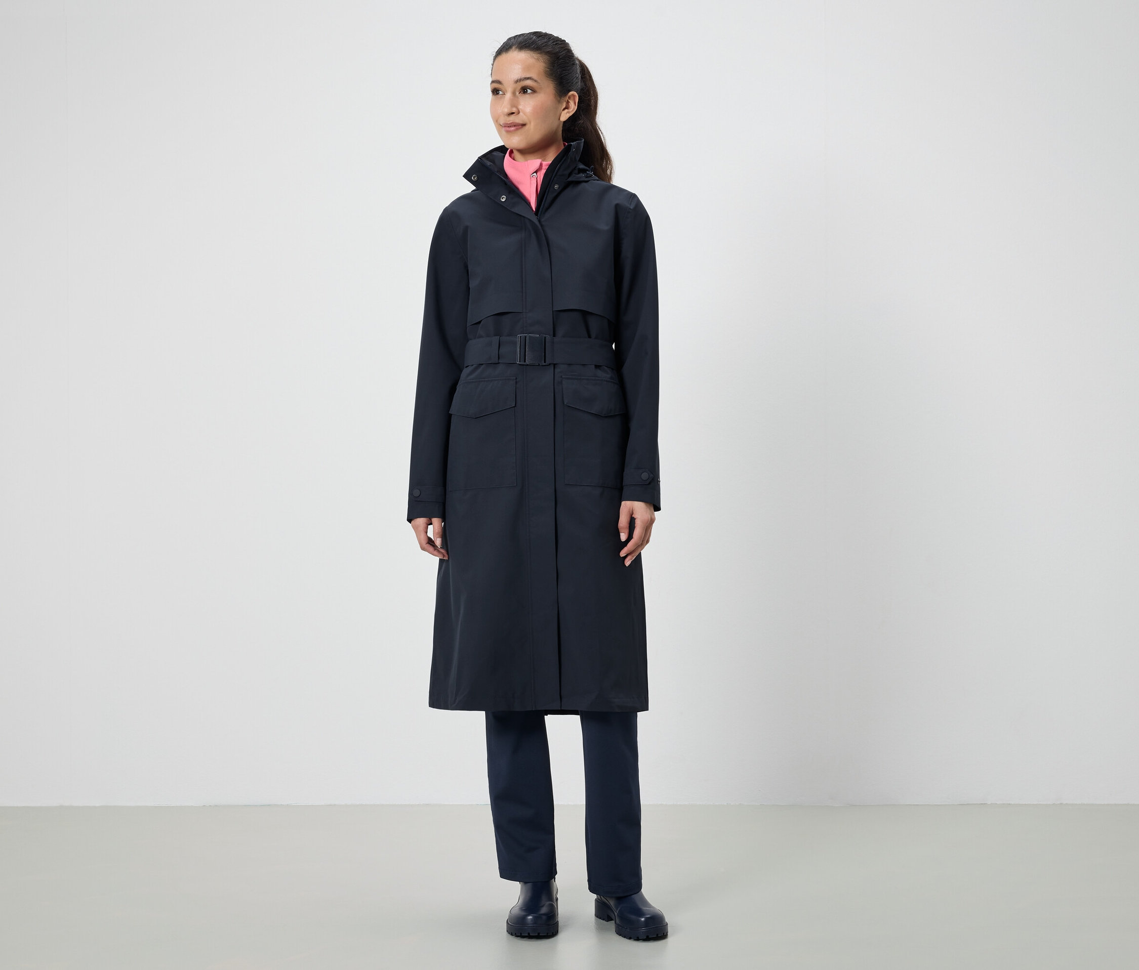 Egy nő hosszú, fekete öves kabátot visel.