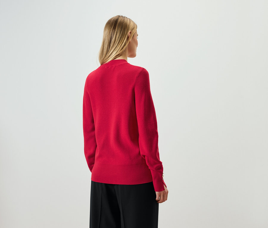 Hátulról látható egy szőke hajú nő piros pulóverben és fekete nadrágban.