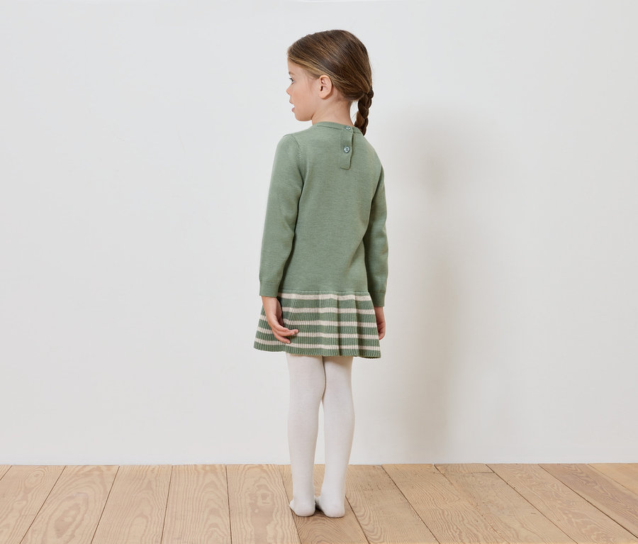 Egy zöld kötött ruhás lány háttal áll a kamerának.