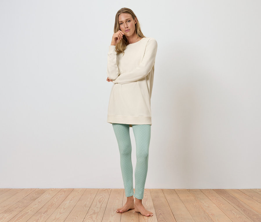 Egy nő áll és pózol egy krémszínű tunikában és világoszöld leggingsben.