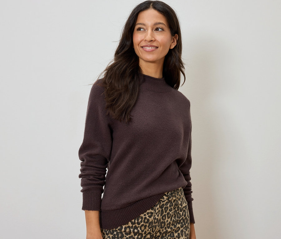 Mosolygó nő barna pulóverben és leopárdmintás szoknyában.