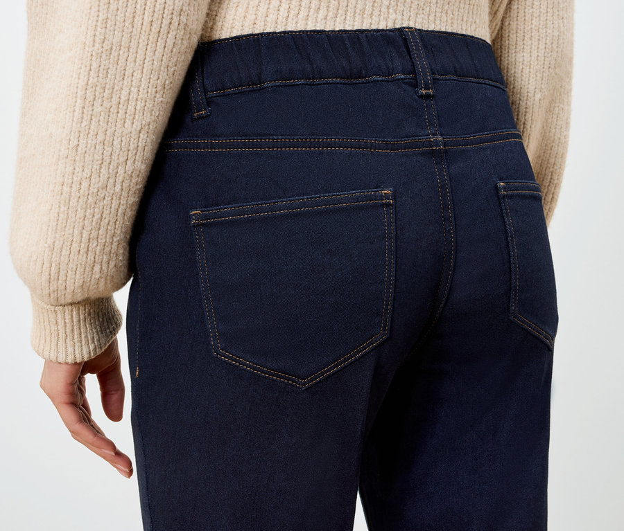 Hátulnézet egy sötétkék jeggingset és bézs pulóvert viselő nőről.