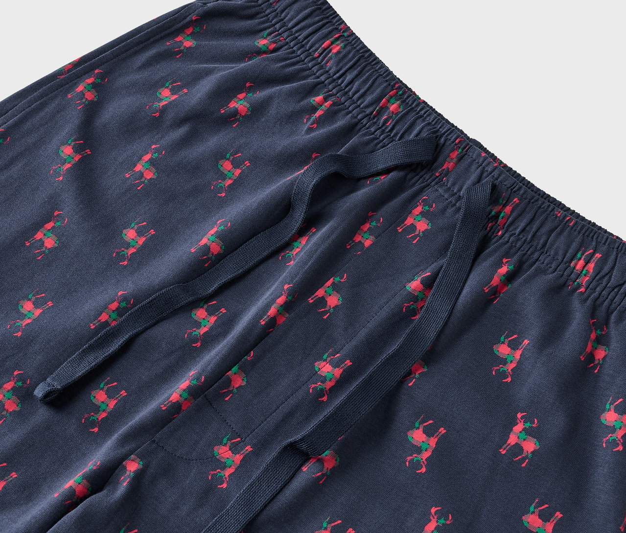 Kék pizsamanadrág részlete piros rénszarvasokkal és zöld nyergekkel.