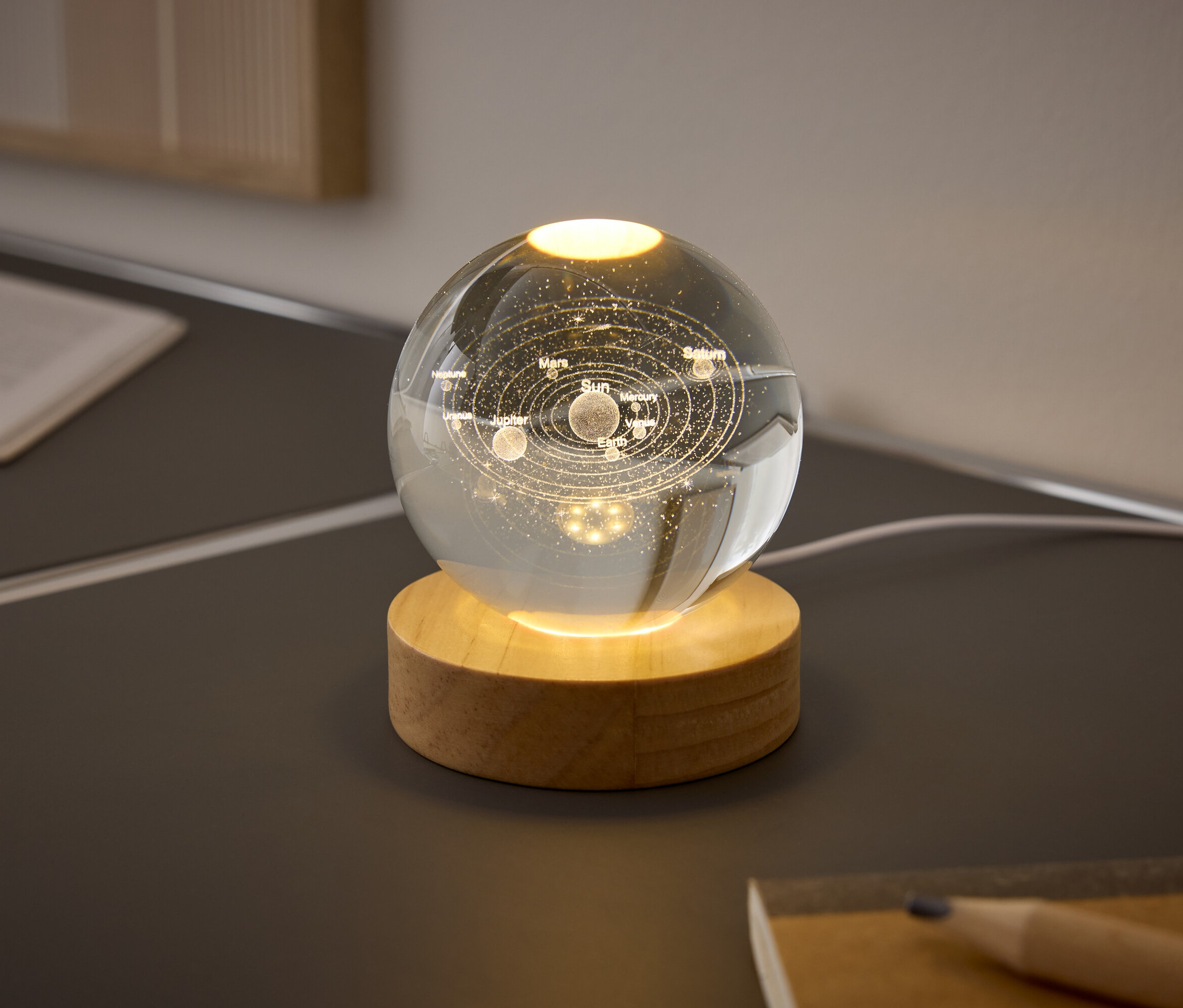 Egy üveggömb a Naprendszer bolygóival egy fa talapzaton világít az asztalon.