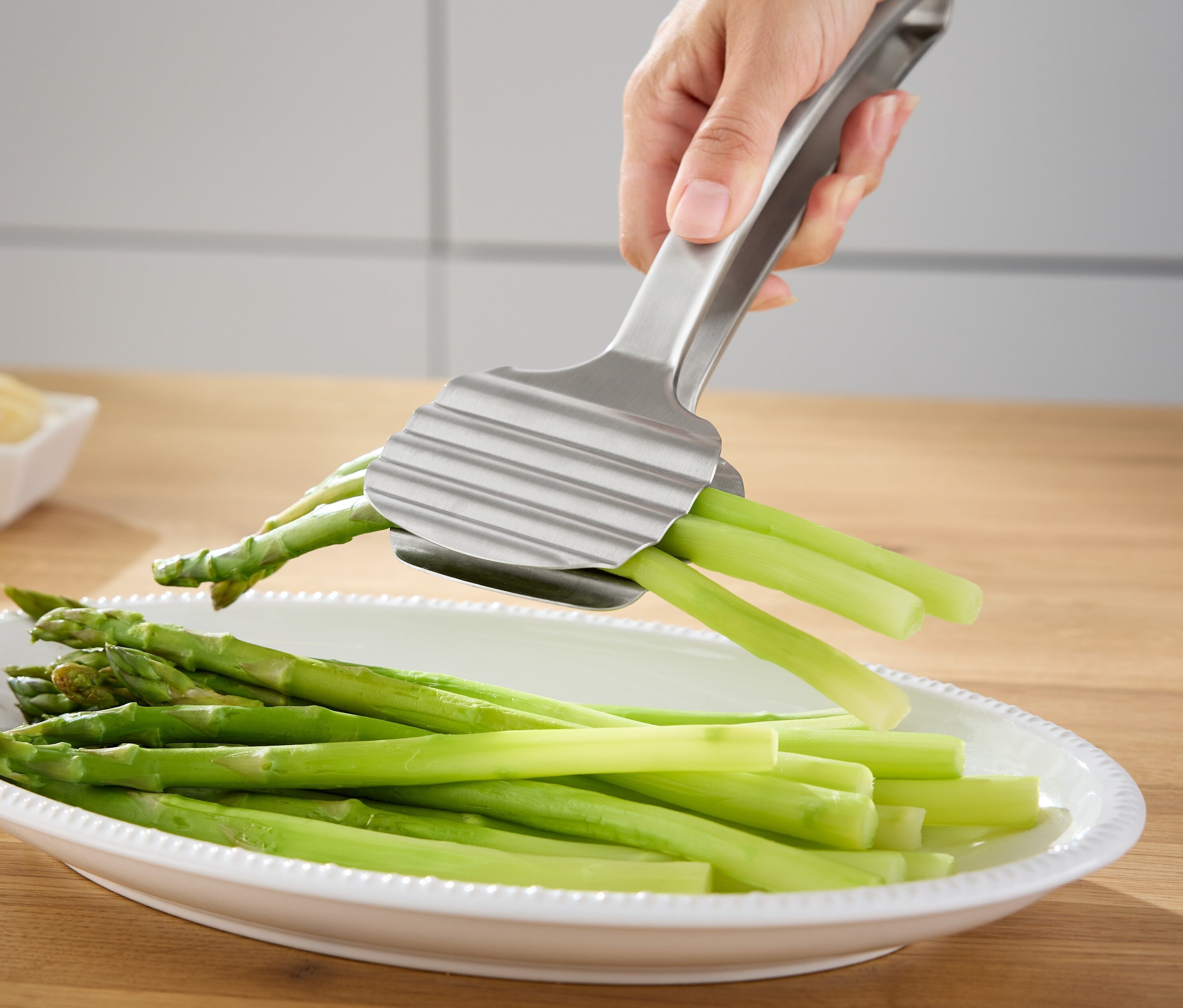 Egy kéz ezüst spárgafogót tart egy tál zöld spárga fölött.