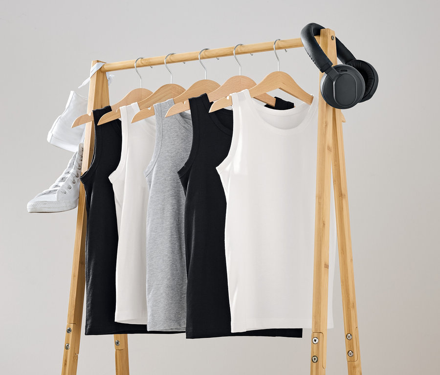 Fekete, fehér és szürke trikók lógnak egy fa állványon. Egy fehér cipő és egy fekete fejhallgató is az állványon van.