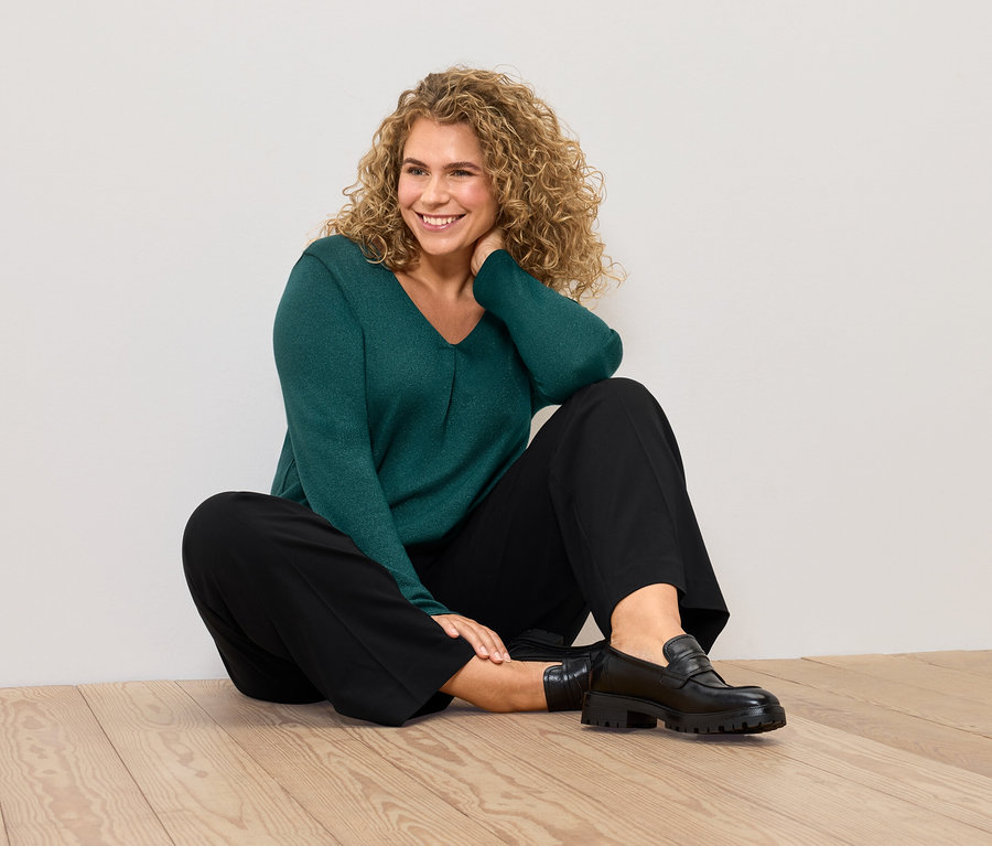 Egy nő ül a padlón zöld pulóverben és fekete nadrágban.