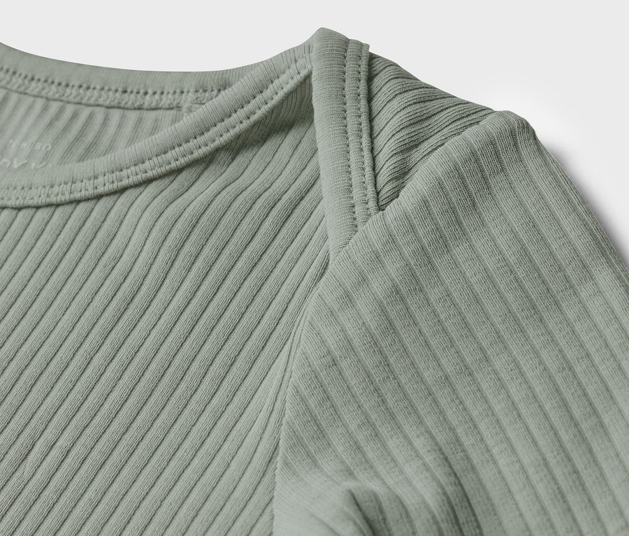 Egy világoszöld, bordázott kisgyerek hosszú ujjú felső részletének közeli képe.