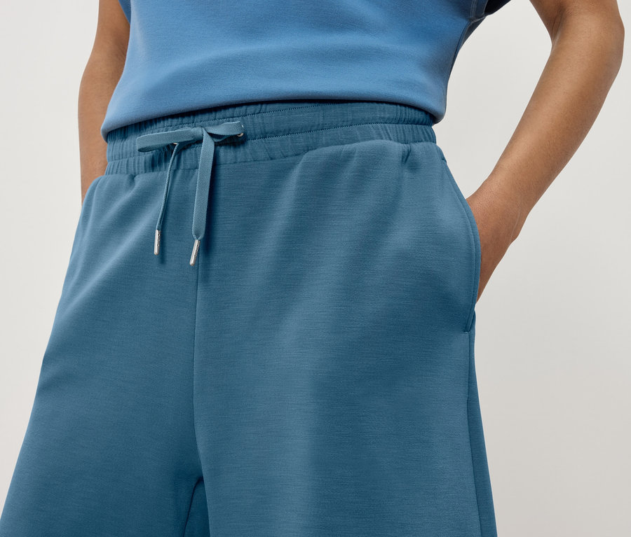 Egy nő részlete látható kék színű szabadidőnadrágban, kezével a zsebében.