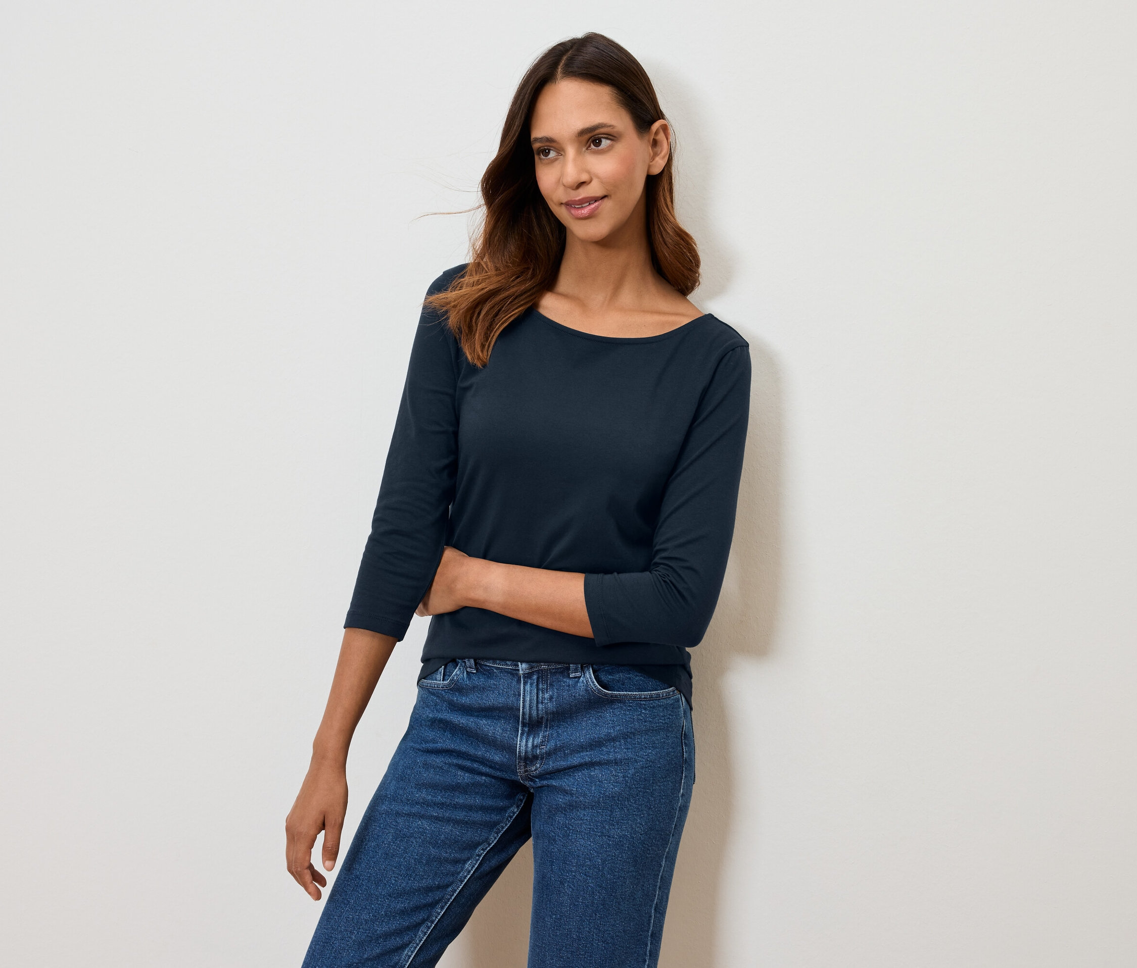 Nő pózol sötétkék háromnegyedes ujjú pólóban és kék farmerben.