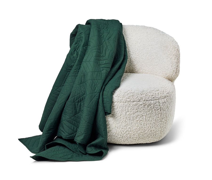 Egy sötétzöld, steppelt ágytakaró (230 x 250 cm) van egy fehér fotelre terítve.