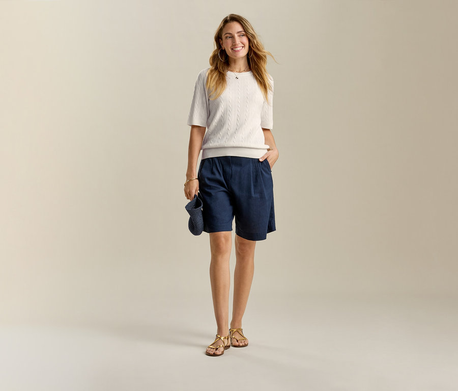 Nő világos felsőben és sötétkék Leinen-Bermuda-Shortsban, egyik kezével a zsebében.