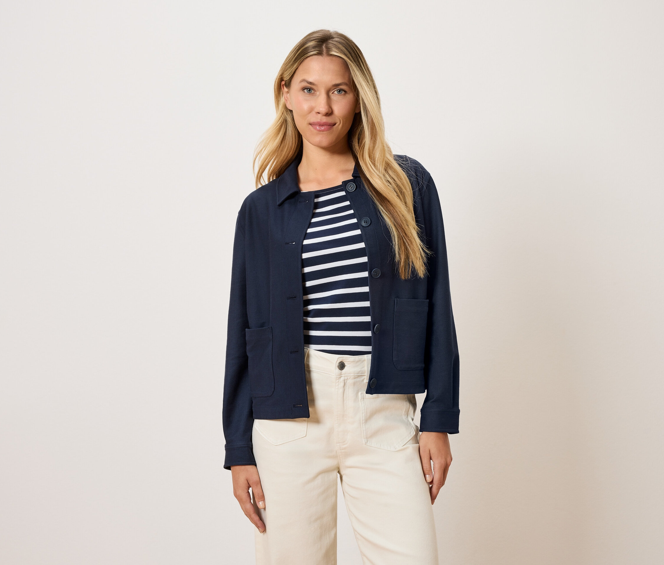 Nő visel egy tengerészkék kabátot egy csíkos felső fölött és krémszínű nadrágot.