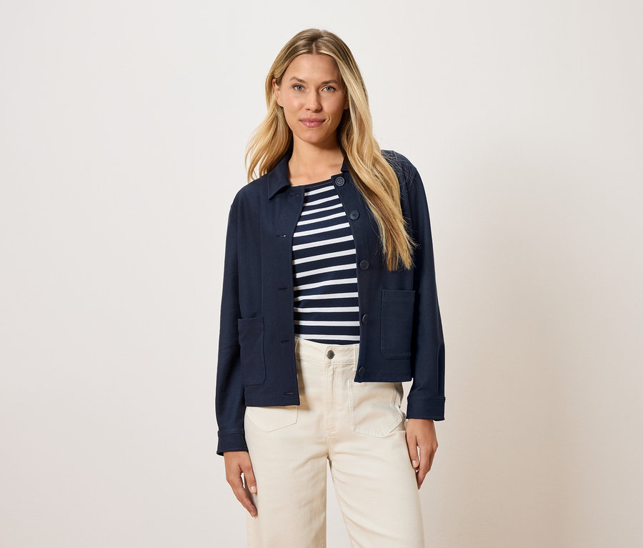 Nő visel egy tengerészkék kabátot egy csíkos felső fölött és krémszínű nadrágot.
