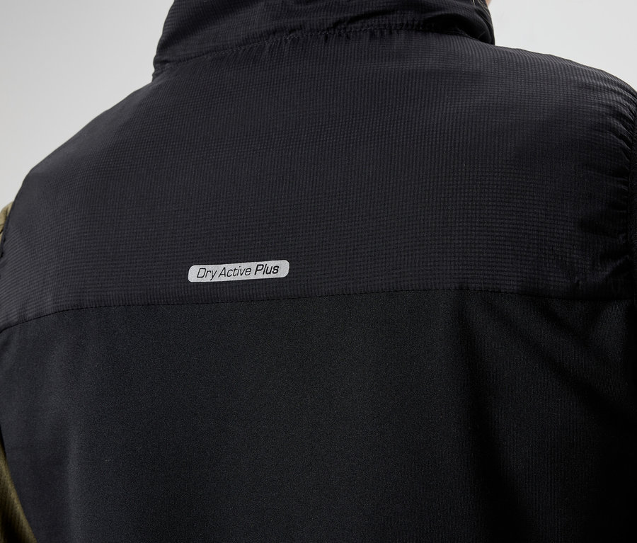 Közeli kép egy fekete mellény hátuljáról, melyen a "Dry Active Plus" felirat látható, egy olívazöld, hosszú ujjú ing felett.
