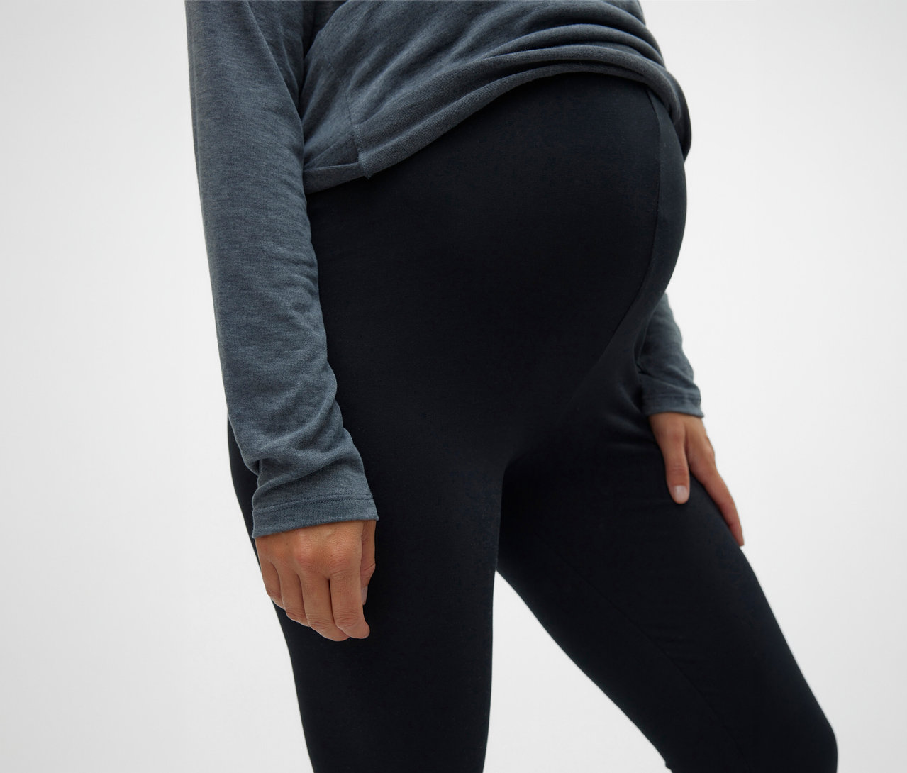 Egy terhes nő MAMALICIOUS 2 db-os fekete leggingset visel egy szürke felső alatt.