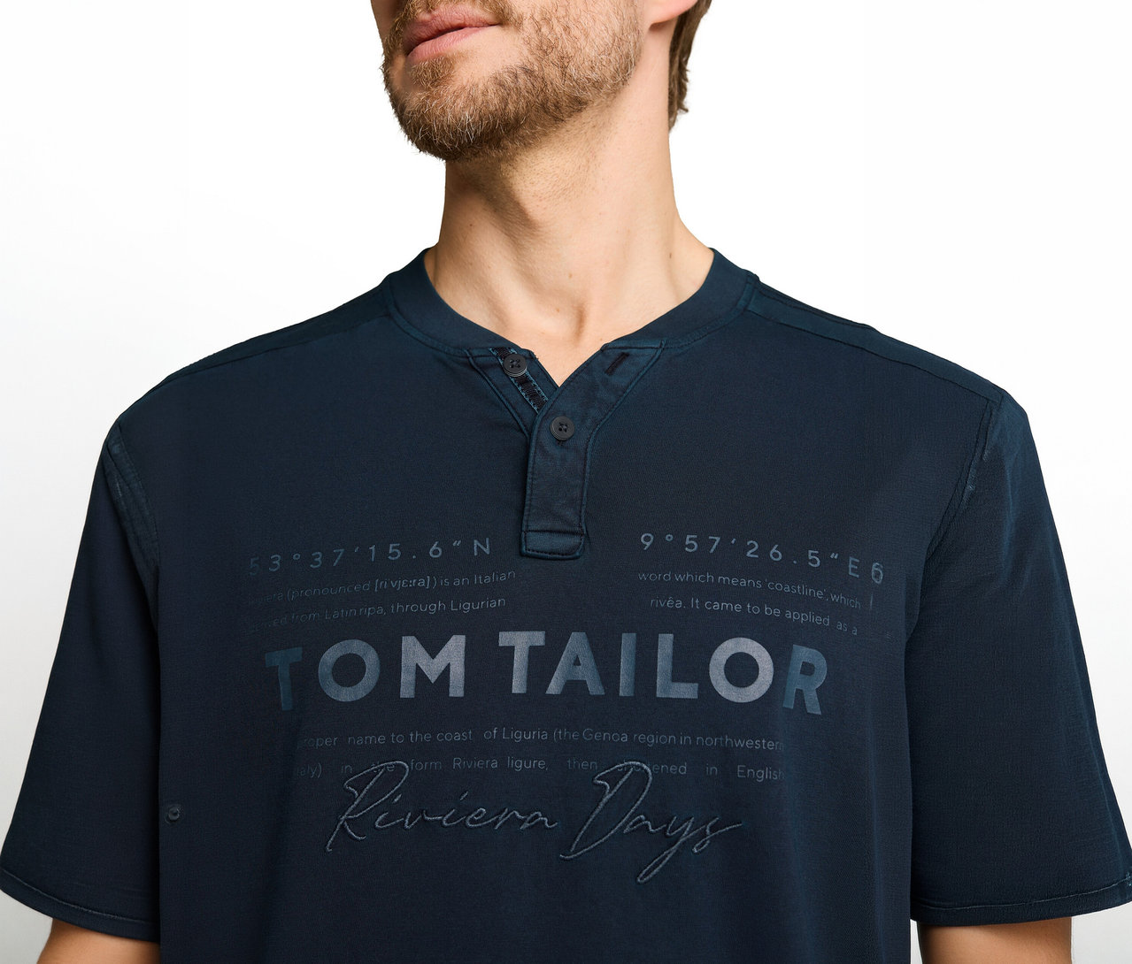 Férfi sötétkék Henley pólót visel, rajta 'TOM TAILOR', 'Riviera Days' felirat és földrajzi koordináták.