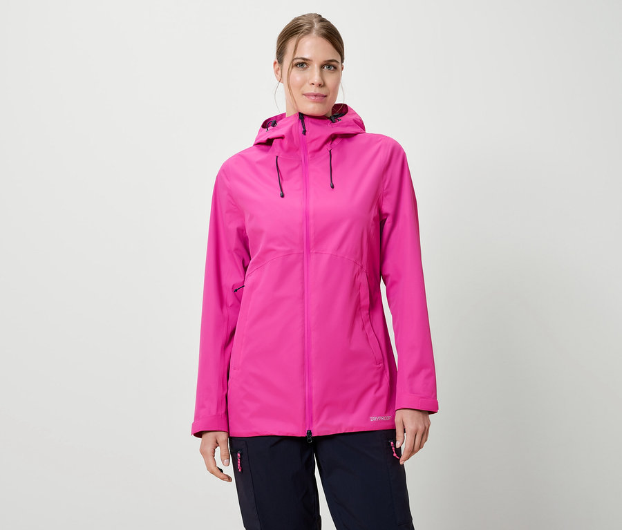Nő visel rózsaszín kapucnis esőkabátot és sötétkék nadrágot fehér háttér előtt.