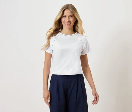 Nő visel fehér pólót és sötétkék culottes-t fehér háttér előtt.