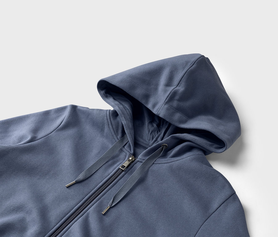 Egy kék, cipzáras kapucnis pulóver közeli képe fehér háttér előtt.