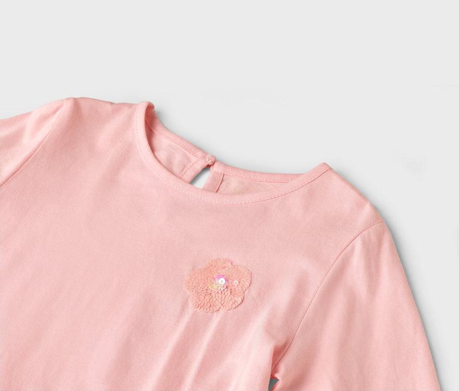 Egy rózsaszín ruha közeli képe flitteres virággal a mellkasán.