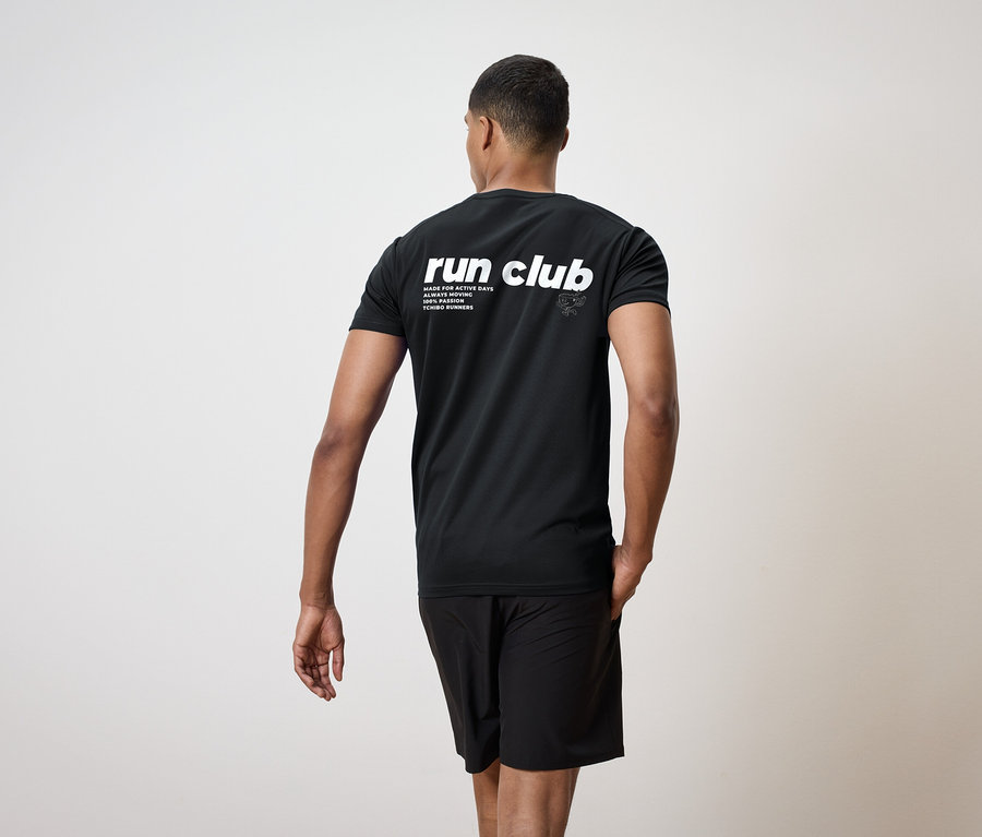 Egy férfi hátulról, fekete pólóban, "run club" felirattal és fekete rövidnadrágban.