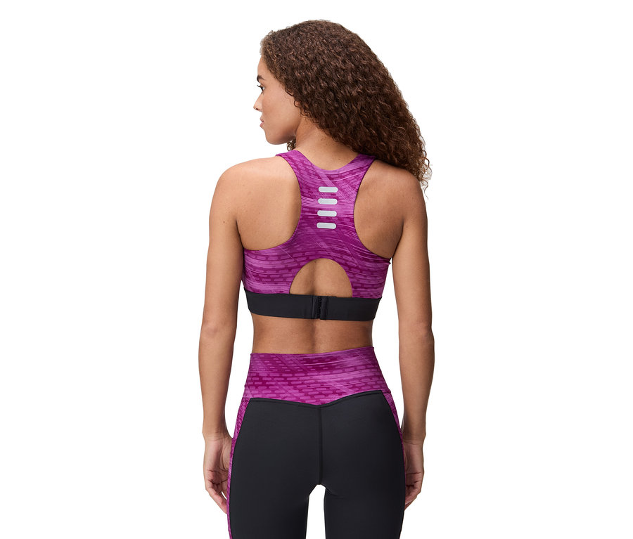 Hátulnézet egy göndör hajú nőről, aki lila-fekete sportmelltartót és leggingset visel.